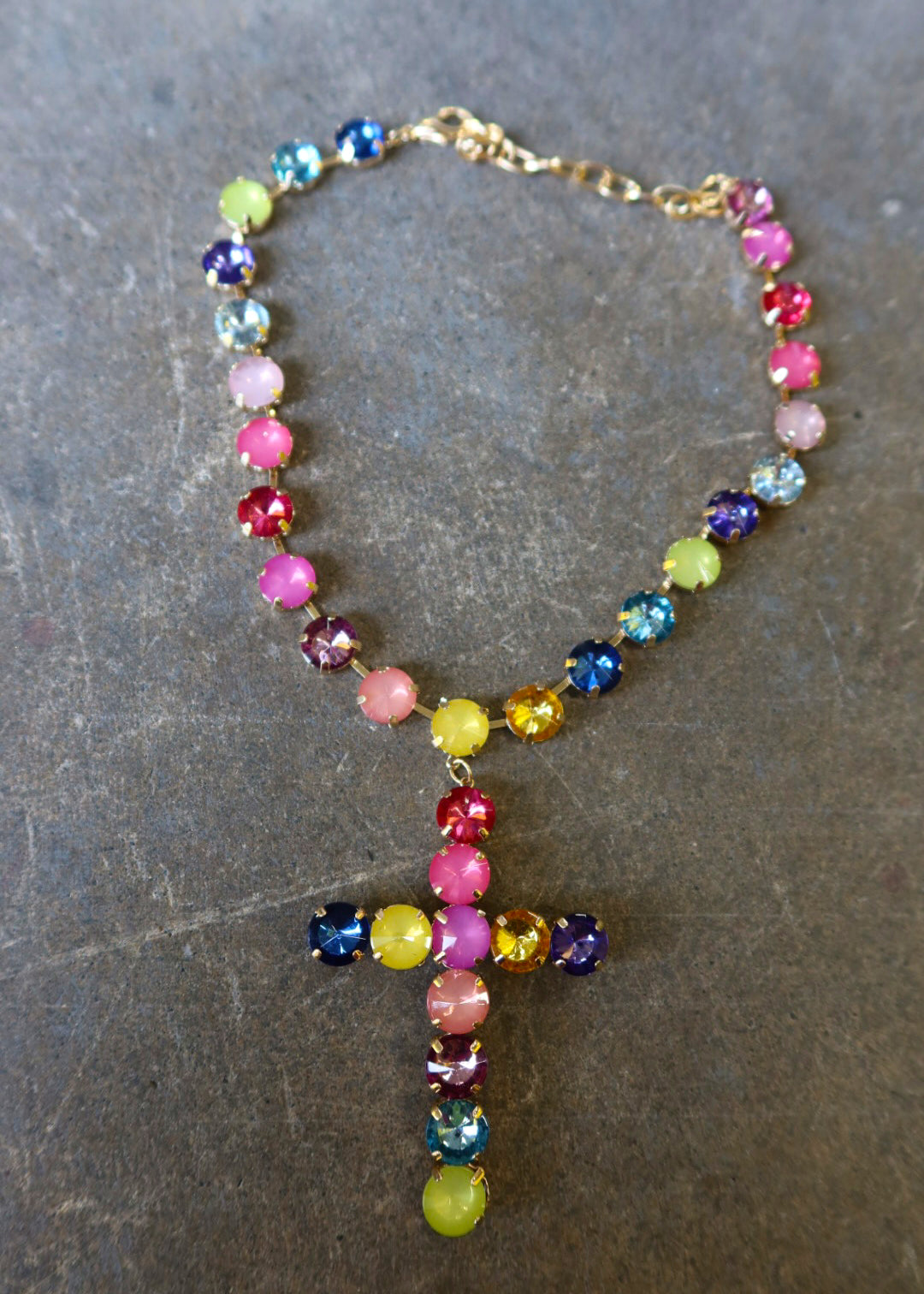 A gold necklace with multi-color jewels and a jeweled cross on a dark surface