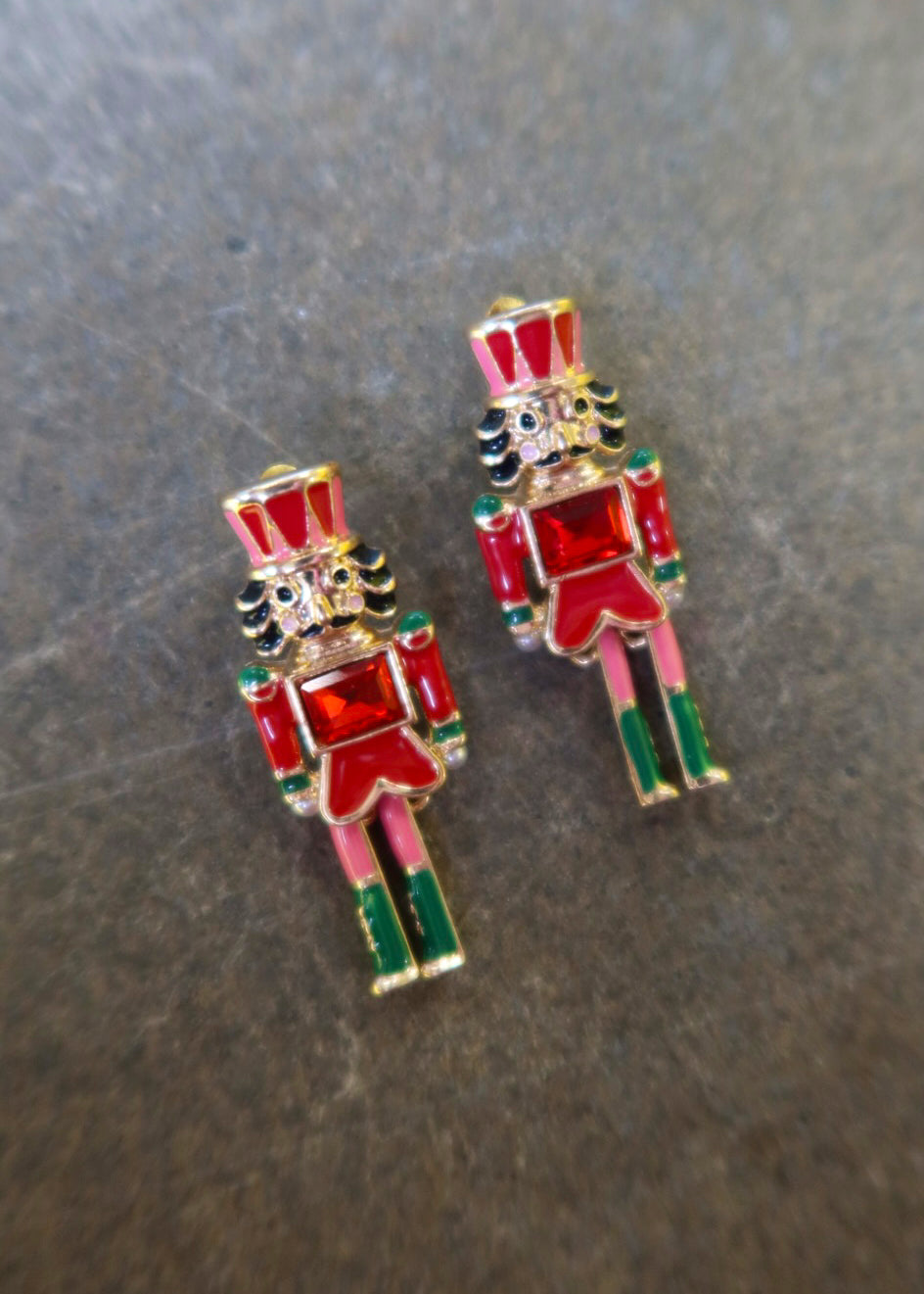 A pair of gold nutcracker earrings on a dark surface