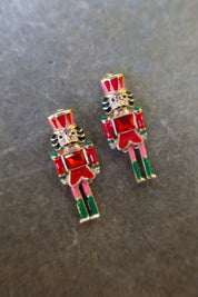 A pair of gold nutcracker earrings on a dark surface