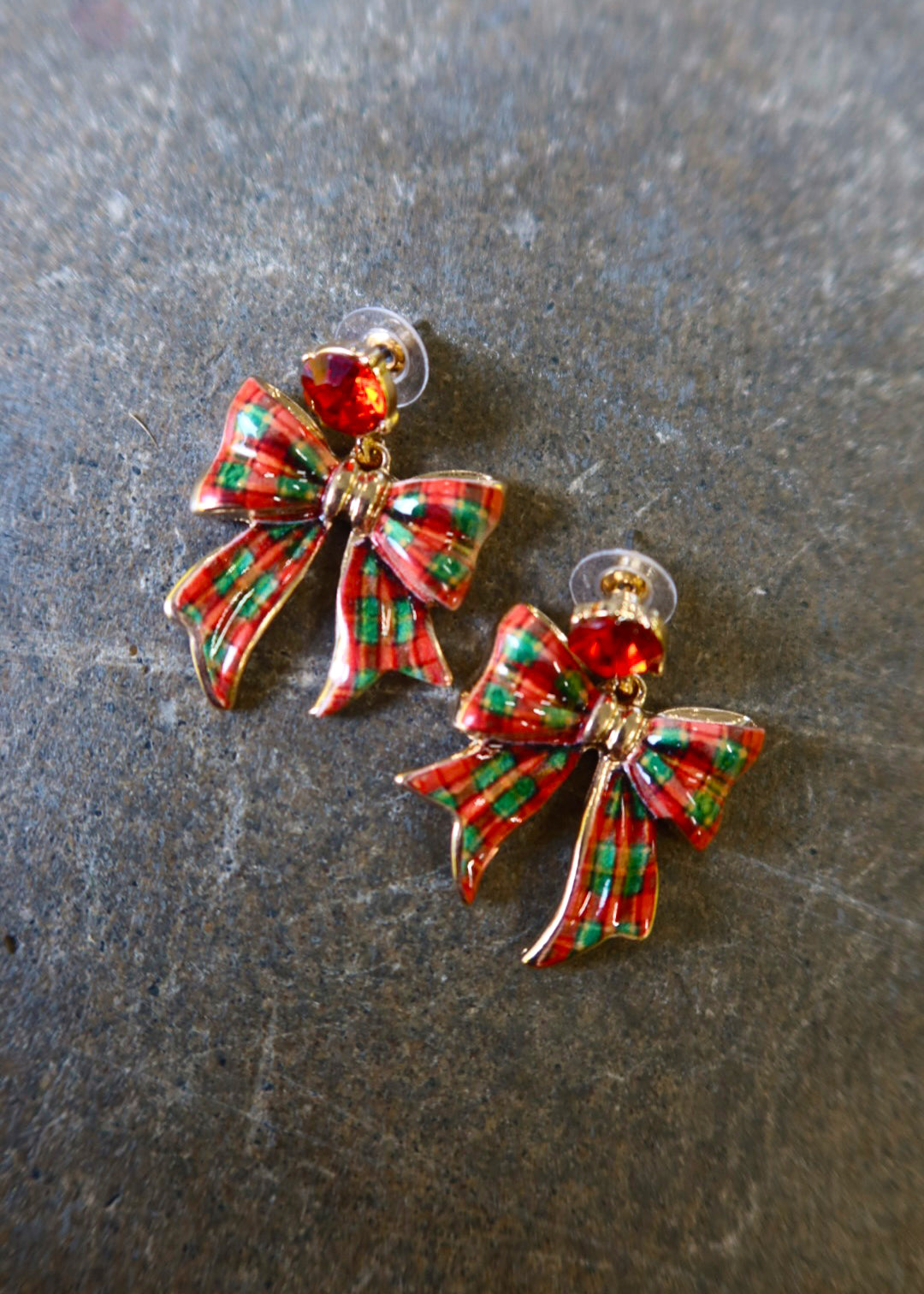 Gold earrings with red and green bows on a dark background