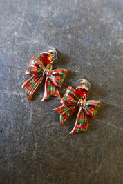 Gold earrings with red and green bows on a dark background