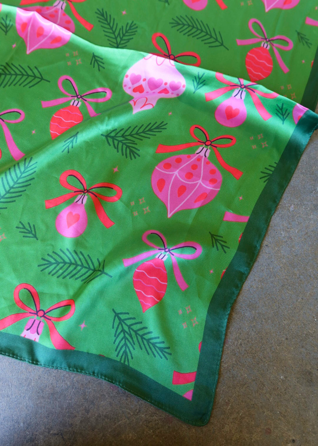A green satin bandana with pink ornament designs on a dark surface
