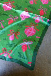 A green satin bandana with pink ornament designs on a dark surface