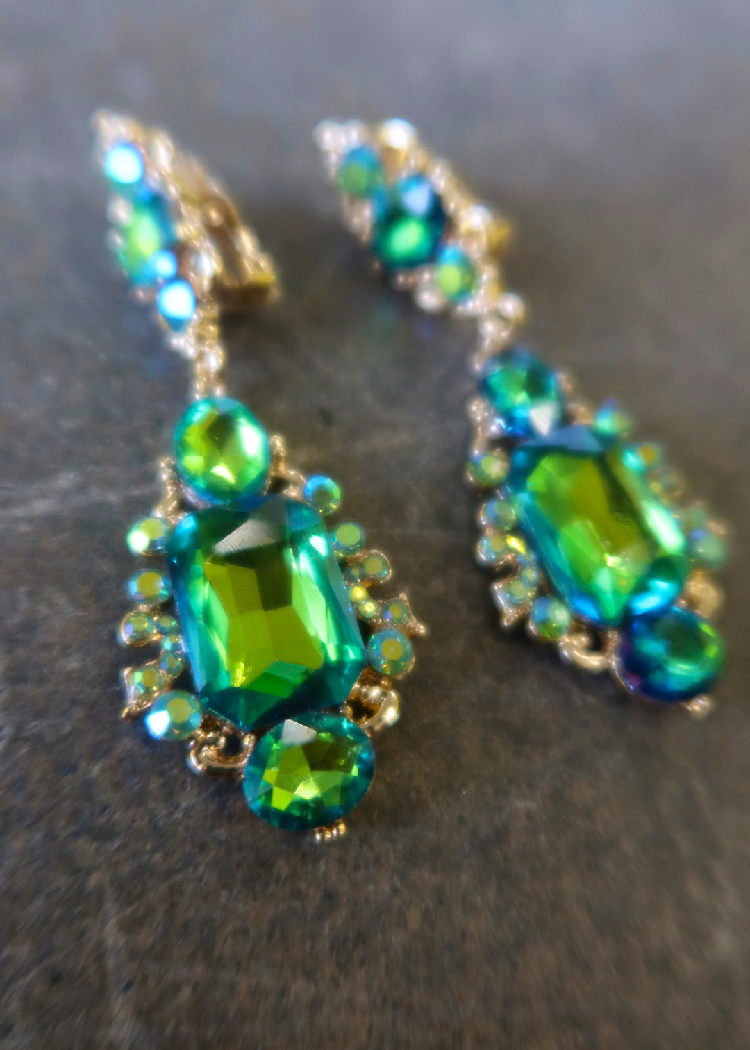 Close up clip on gold earrings with green jewels on a dark surface