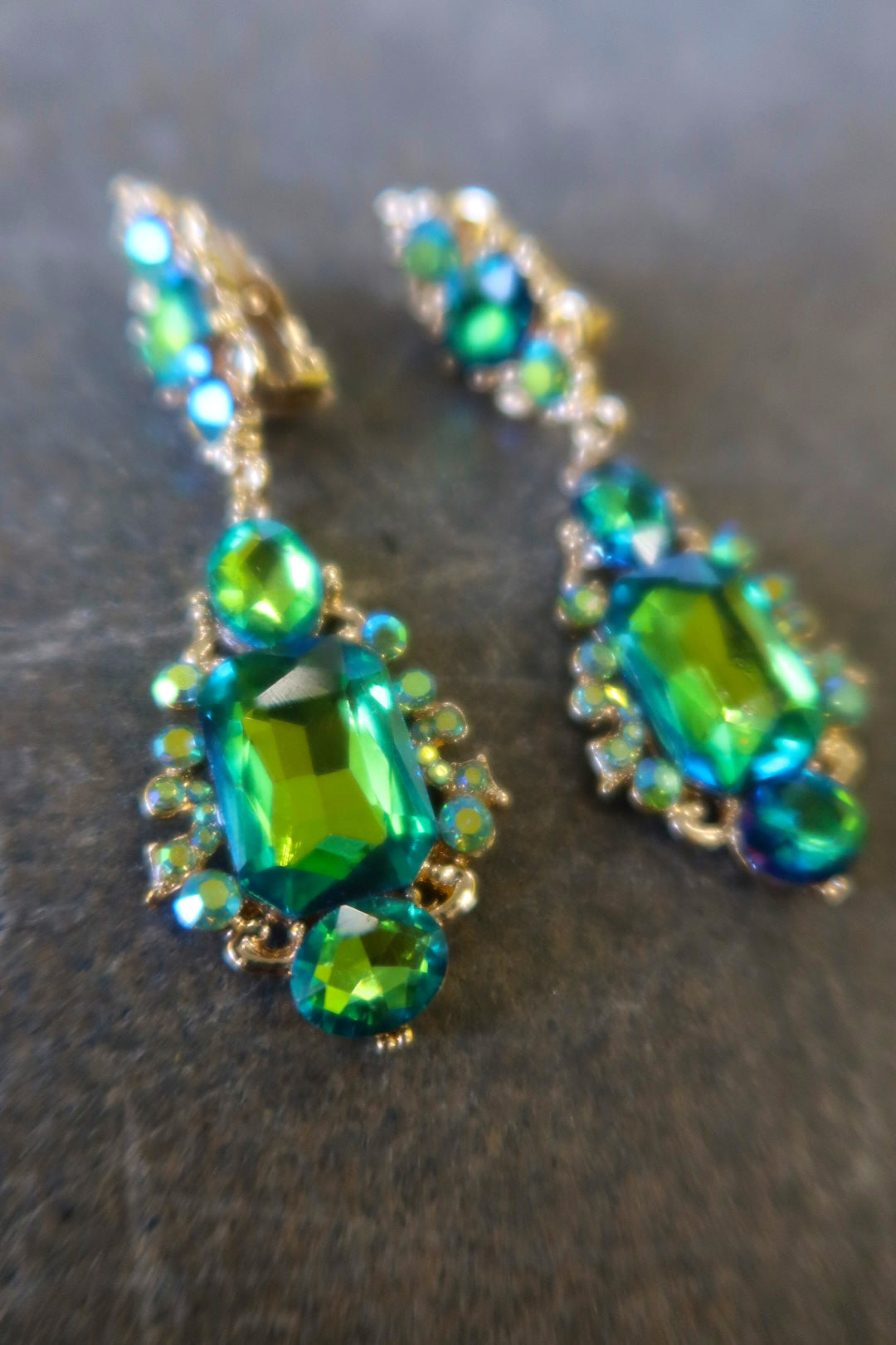 Close up clip on gold earrings with green jewels on a dark surface