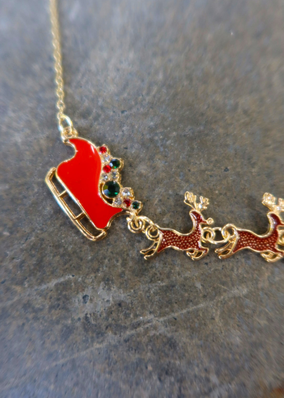 Close up of a gold necklace with Santa's sleigh and reindeer in red on a dark surface