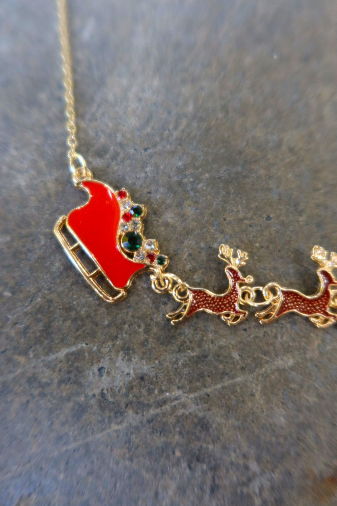 Close up of a gold necklace with Santa's sleigh and reindeer in red on a dark surface