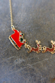 Close up of a gold necklace with Santa's sleigh and reindeer in red on a dark surface
