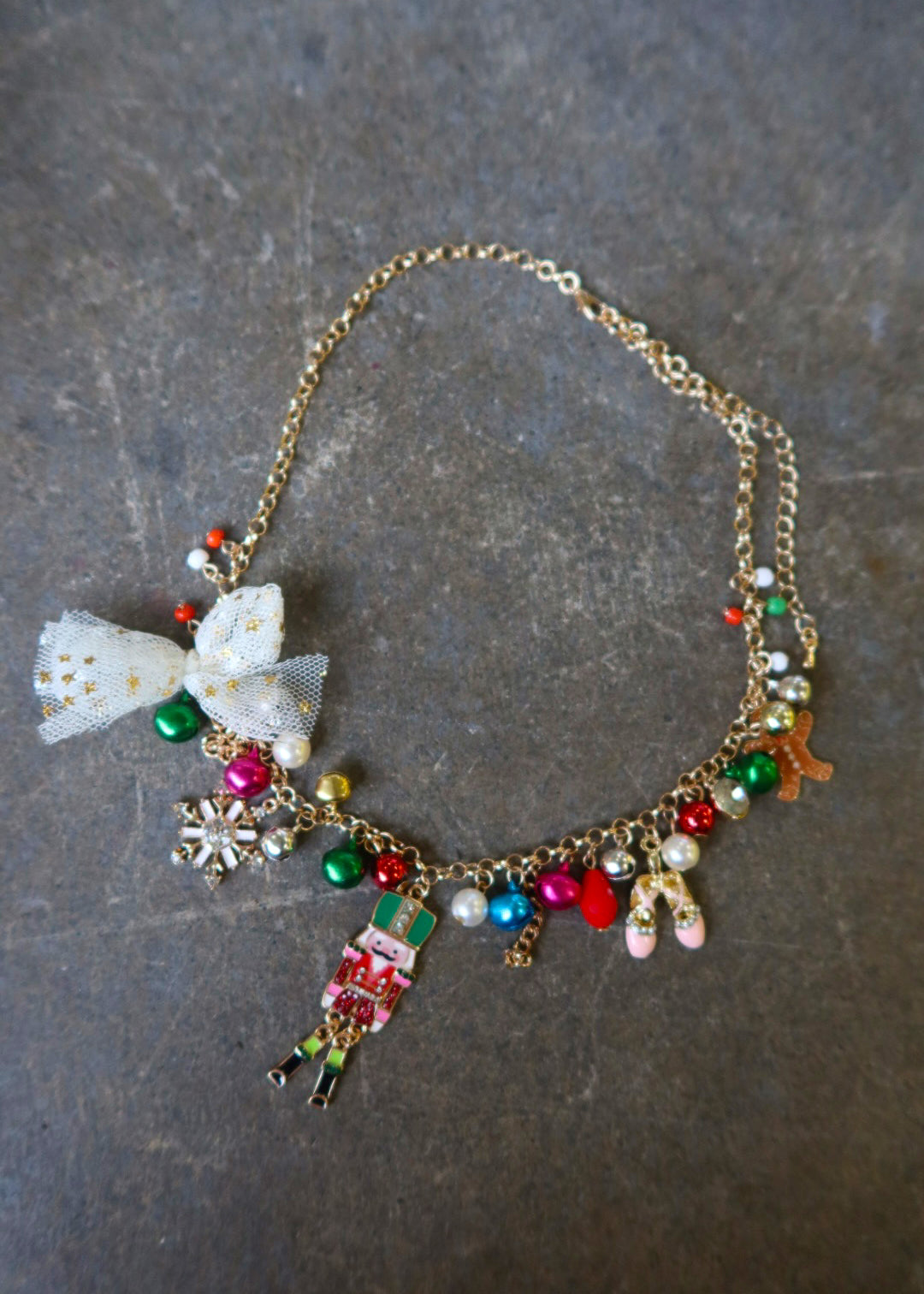 A gold necklace with multicolor jewels and a nutcracker and white bow on a dark surface