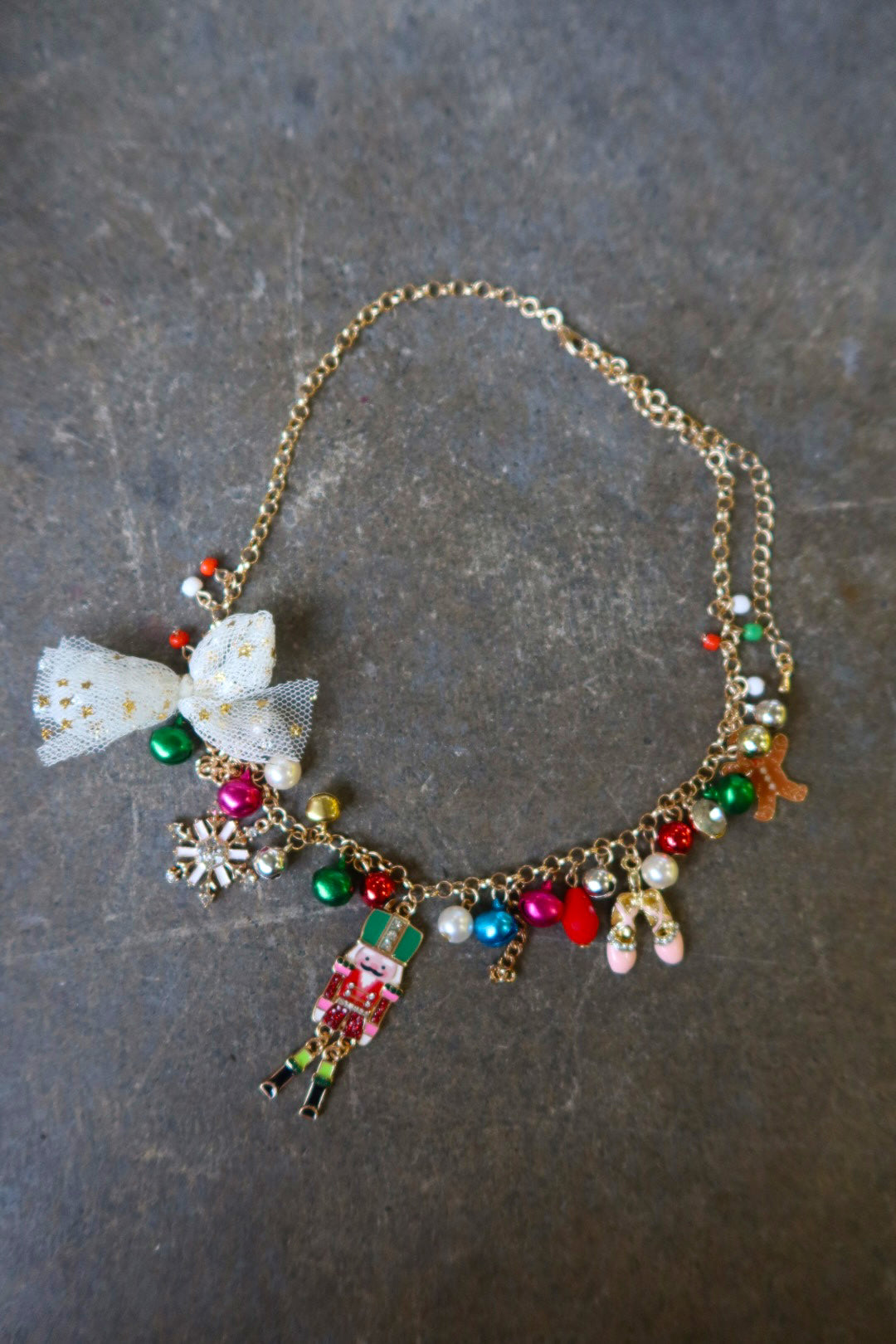 A gold necklace with multicolor jewels and a nutcracker and white bow on a dark surface