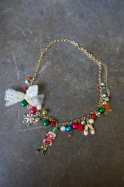 A gold necklace with multicolor jewels and a nutcracker and white bow on a dark surface