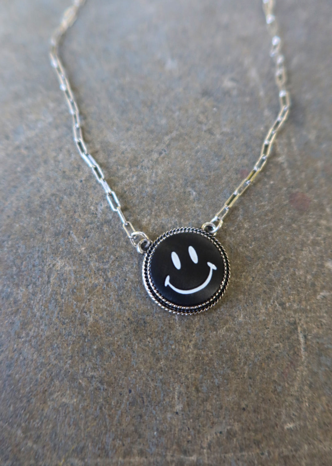 Close up of a silver necklace with a black smiley face charm on a dark surface