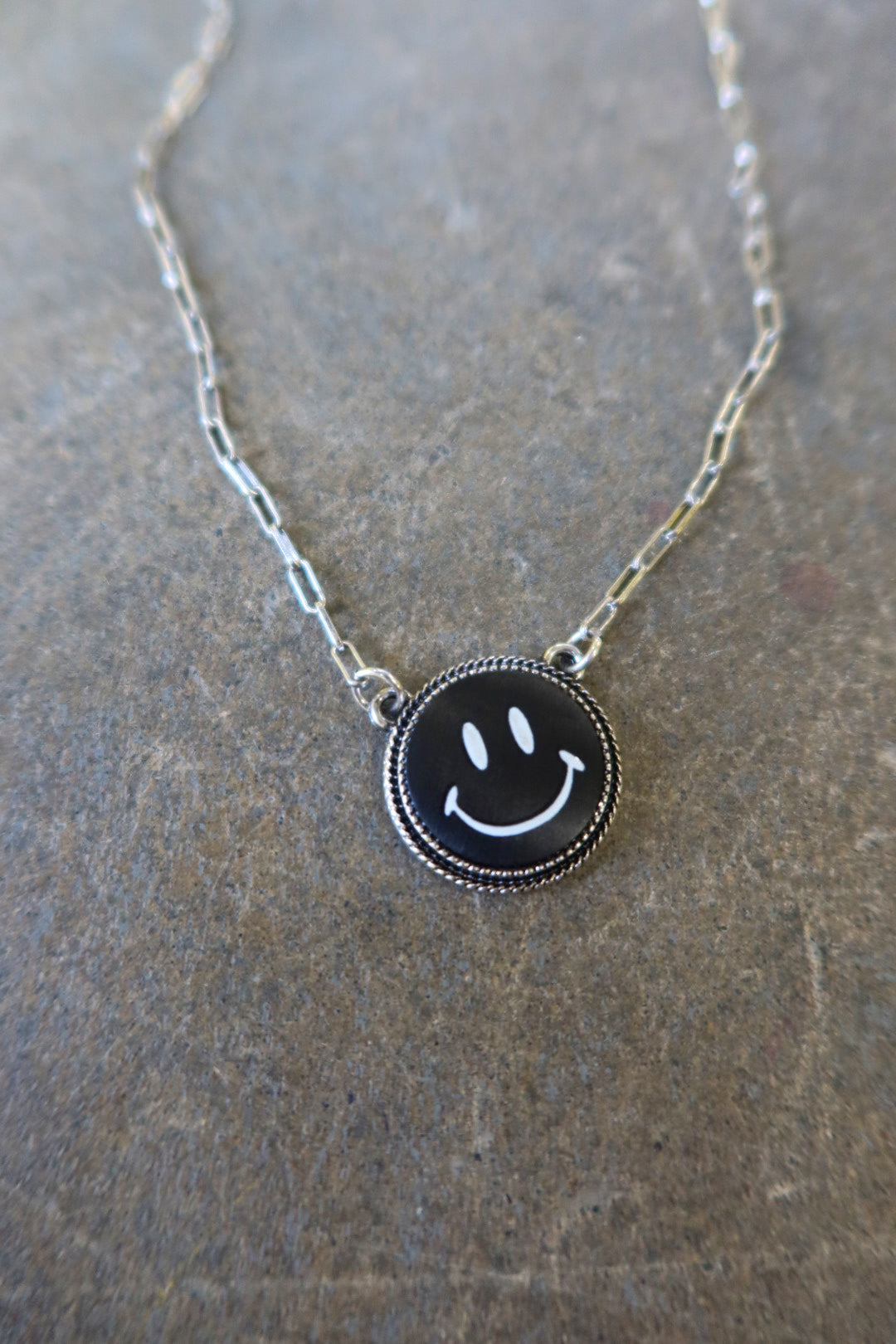 Close up of a silver necklace with a black smiley face charm on a dark surface
