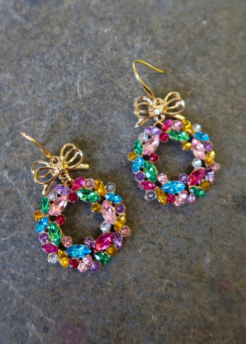 Pair of gold earrings with multicolored wreaths on a dark surface