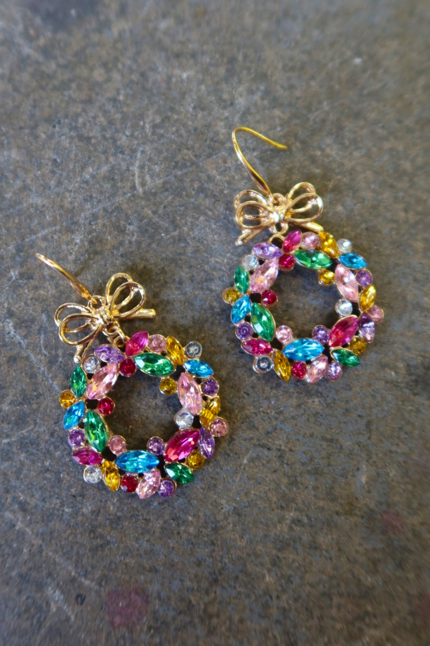 Pair of gold earrings with multicolored wreaths on a dark surface