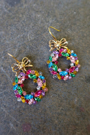 Pair of gold earrings with multicolored wreaths on a dark surface
