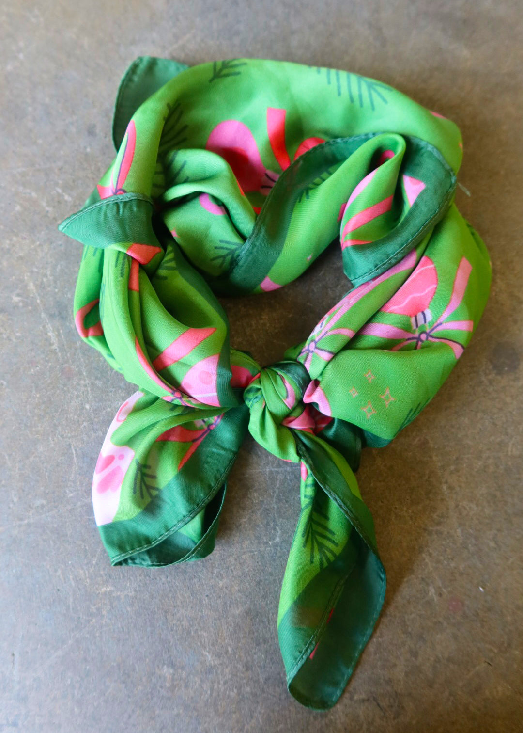 A green satin bandana tied with pink designs on a dark surface
