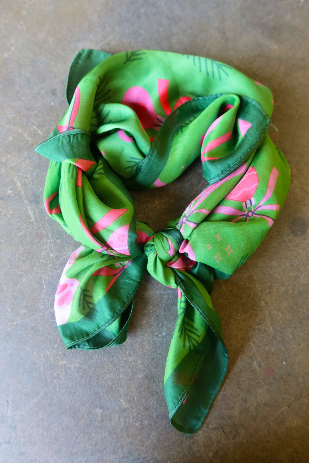 A green satin bandana tied with pink designs on a dark surface