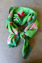 A green satin bandana tied with pink designs on a dark surface