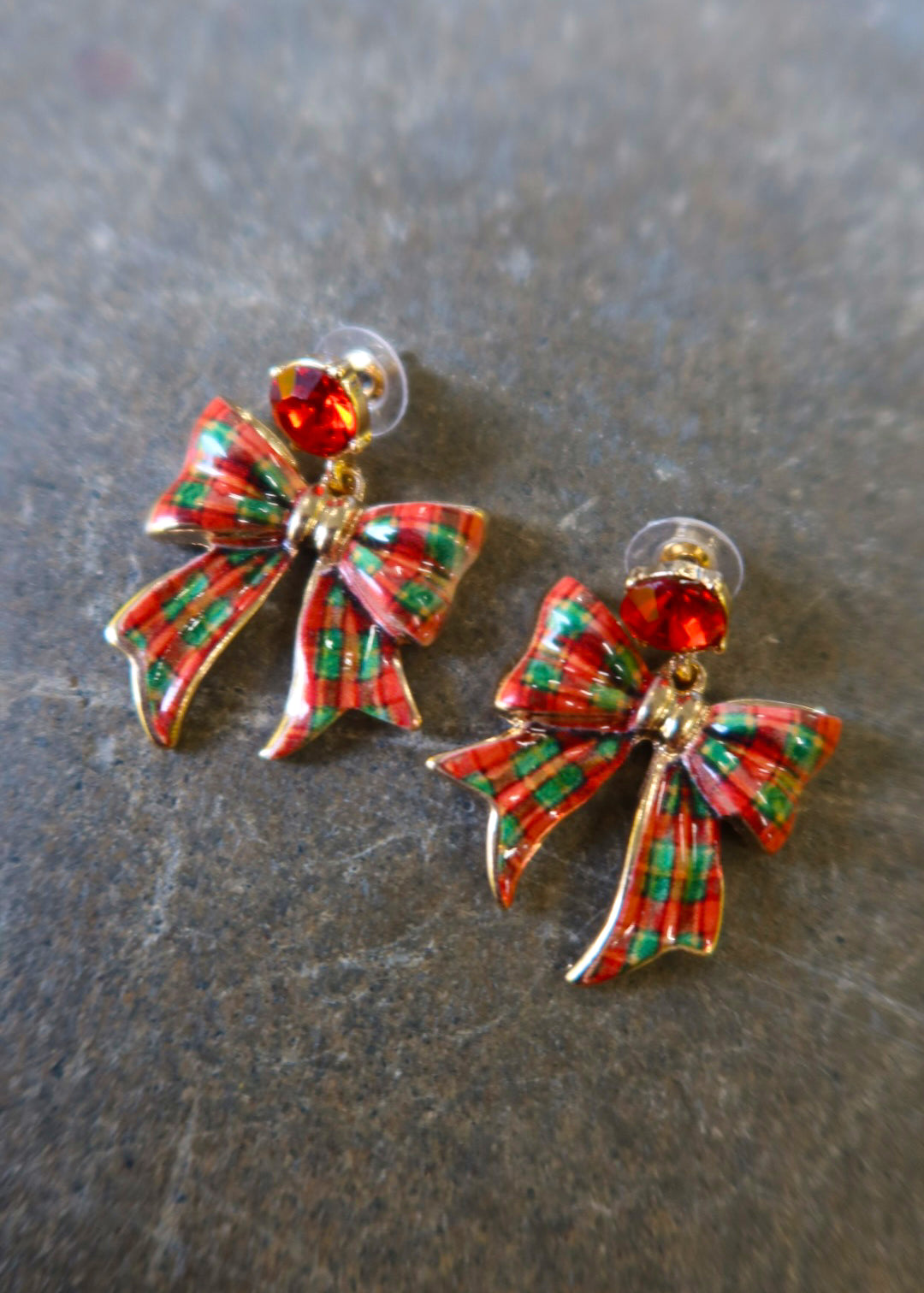 Close up of gold earrings with red and green bows on a dark background
