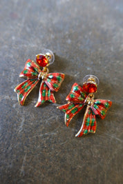 Close up of gold earrings with red and green bows on a dark background