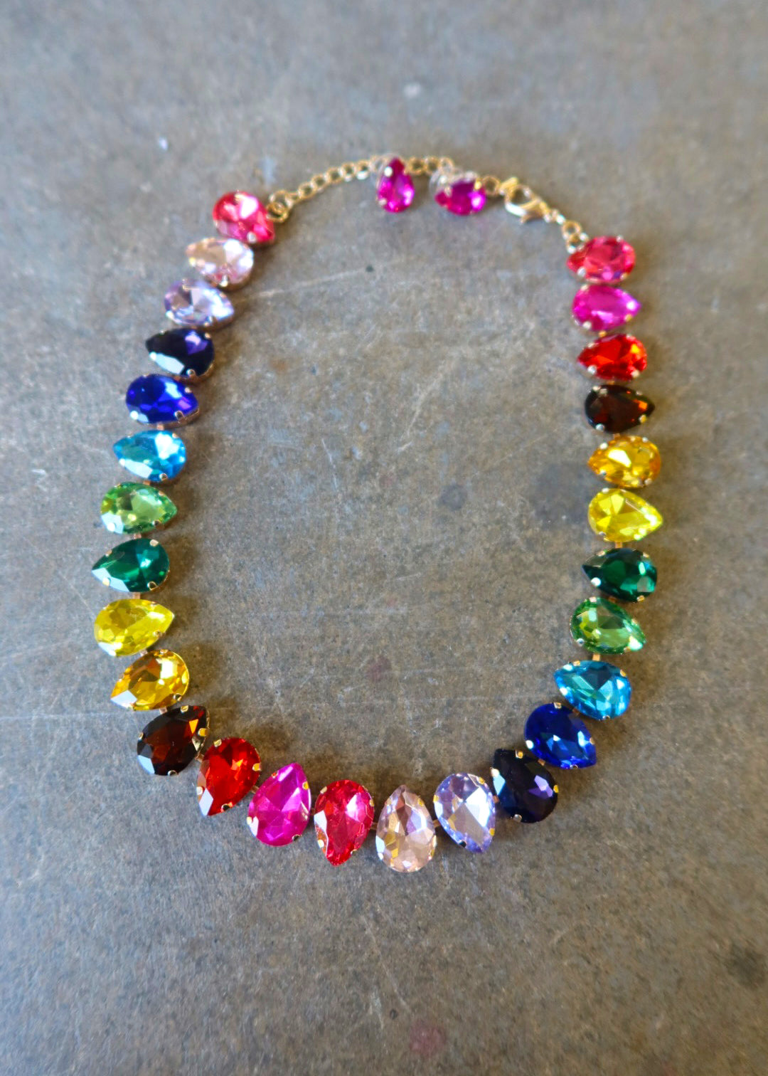 A multi-colored bejeweled gold necklace with matching pink stud earrings on a dark surface