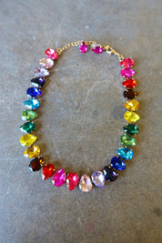A multi-colored bejeweled gold necklace with matching pink stud earrings on a dark surface