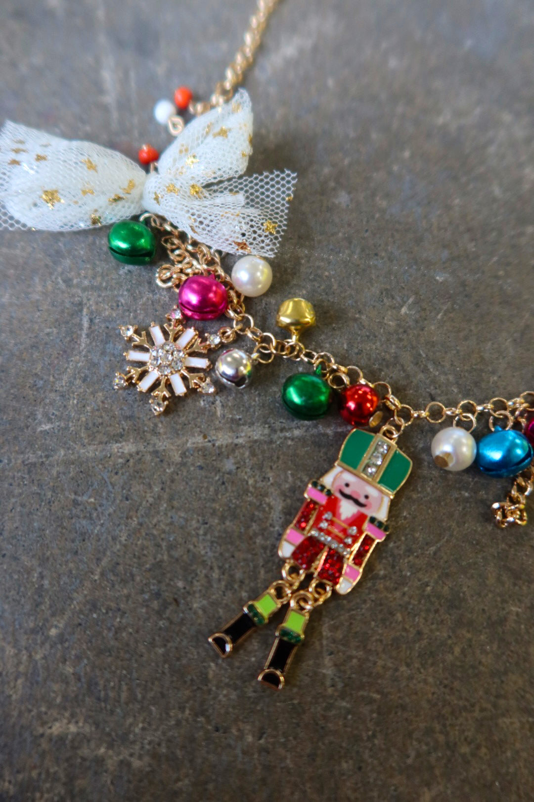 Close up of a gold necklace with multicolor jewels and a nutcracker and white bow on a dark surface
