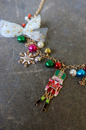 Close up of a gold necklace with multicolor jewels and a nutcracker and white bow on a dark surface