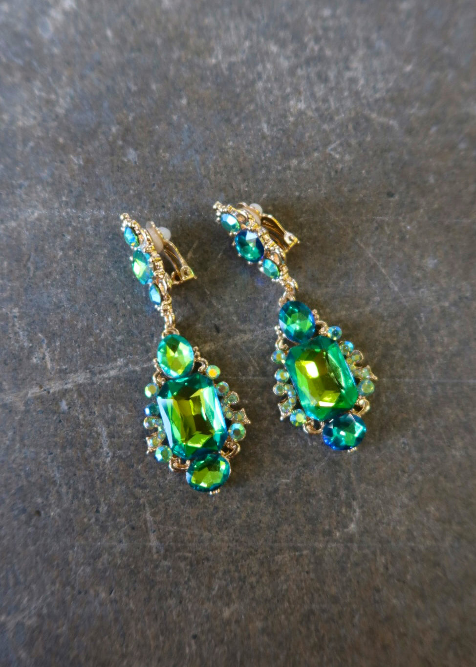 Clip on gold earrings with green jewels on a dark surface