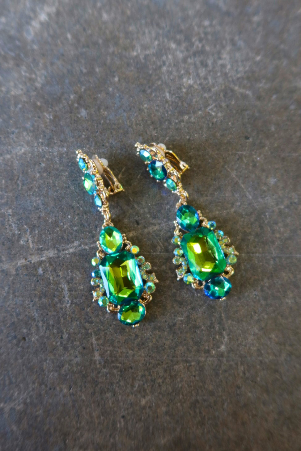 Clip on gold earrings with green jewels on a dark surface