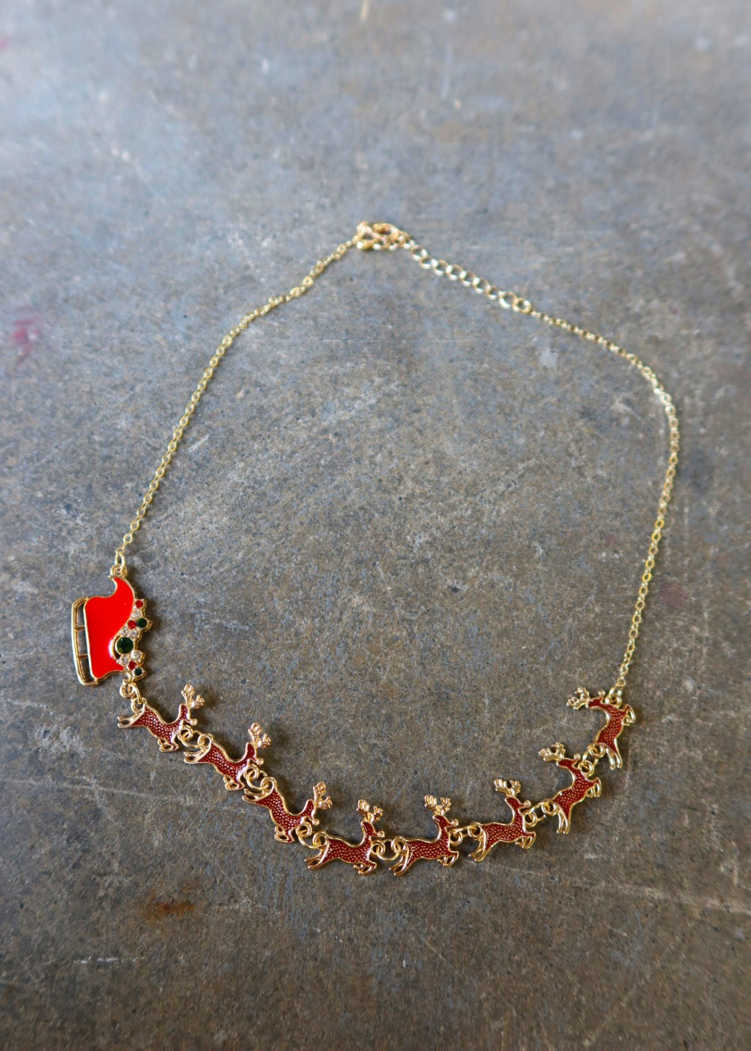 A gold necklace with Santa's sleigh and reindeer in red on a dark surface