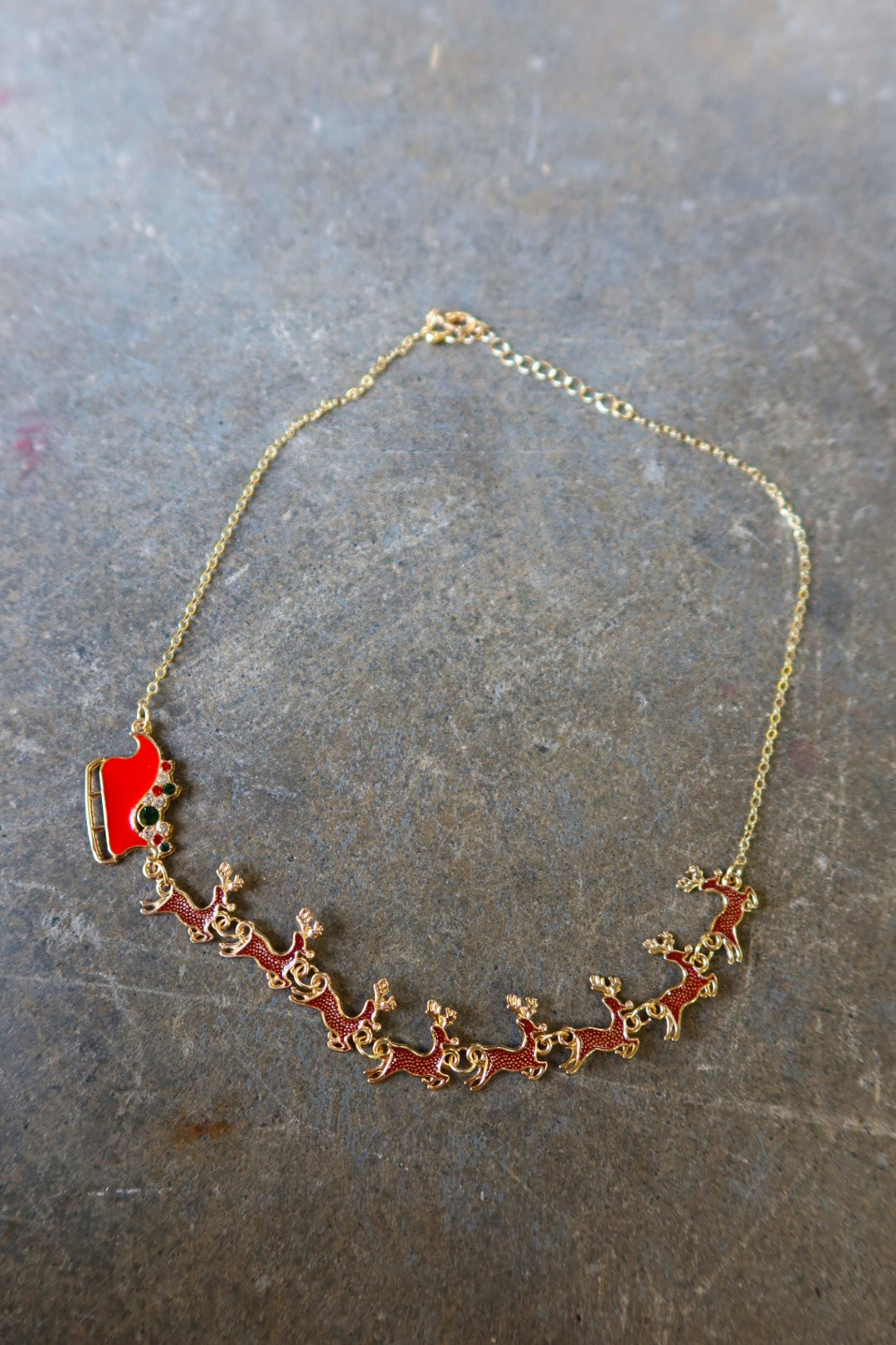 A gold necklace with Santa's sleigh and reindeer in red on a dark surface