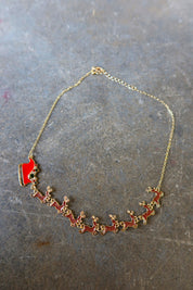 A gold necklace with Santa's sleigh and reindeer in red on a dark surface