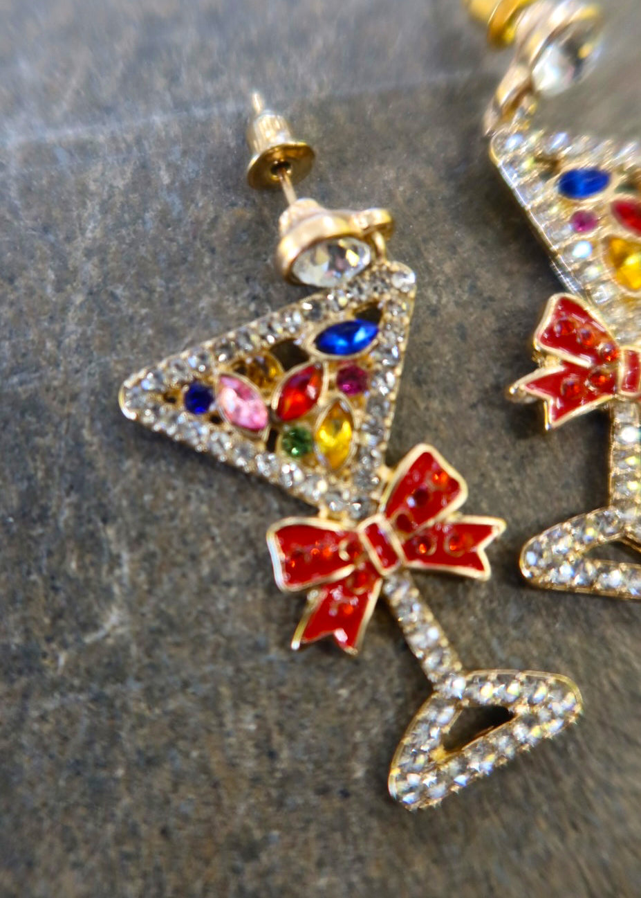 Close up of a pair of silver martini glass earrings with jewels and red bows on a dark background