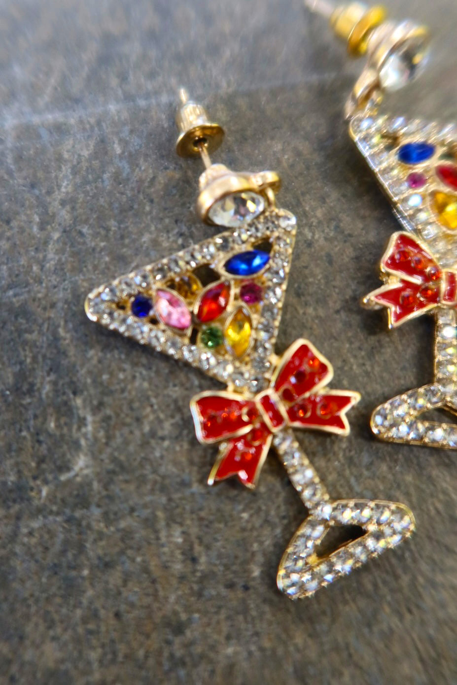 Close up of a pair of silver martini glass earrings with jewels and red bows on a dark background