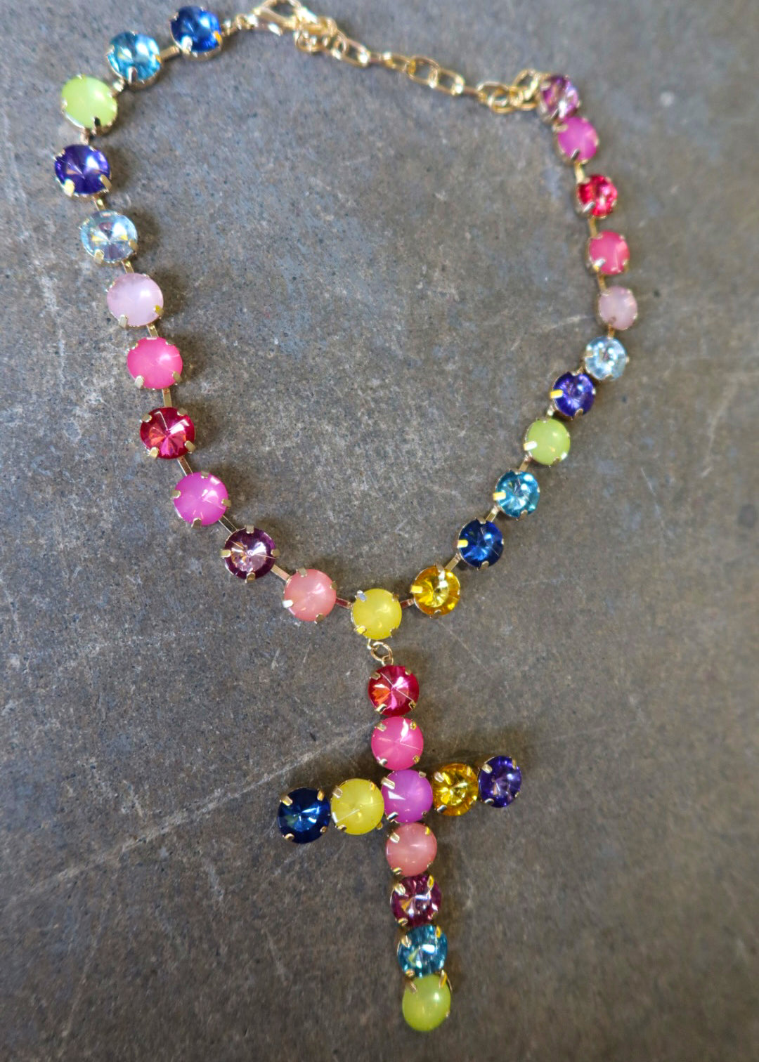A gold necklace with multi-color jewels and a jeweled cross on a dark surface