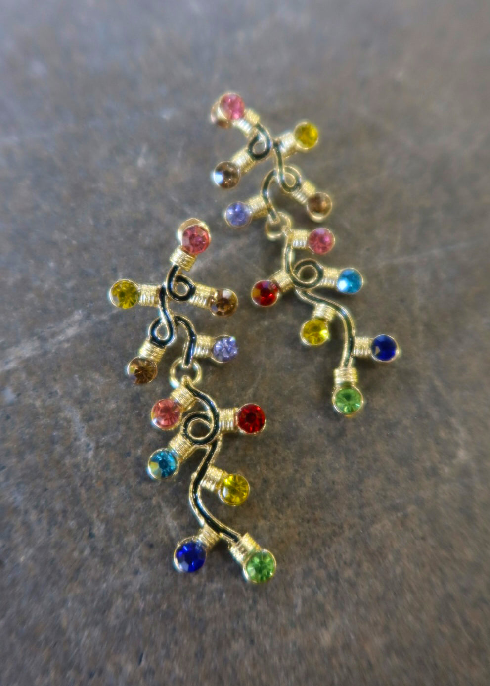 Pair of gold dangly earrings with a string of lights with multi-colored studs on a dark background