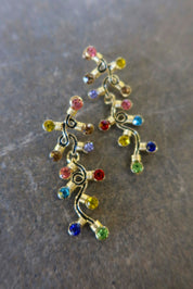 Pair of gold dangly earrings with a string of lights with multi-colored studs on a dark background