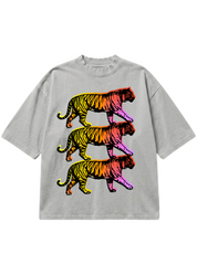A light gray oversized short-sleeve t-shirt featuring a graphic print of three stacked walking tigers in a vibrant rainbow gradient of yellow, orange, red, pink, and purple, displayed flat against a solid white background