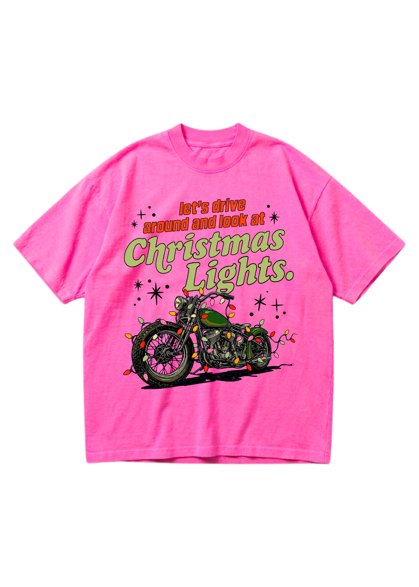 A bright pink oversized graphic tee featuring a vintage motorcycle wrapped in colorful Christmas lights with the text “let’s drive around and look at Christmas Lights.” in orange and green lettering with star accents. Flat lay on white background.