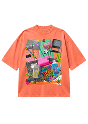 A coral orange short-sleeve t-shirt with a large, colorful graphic collage on the front featuring various fashion and beauty items like a pink laptop, leopard print notebook, makeup palettes, and a hairbrush