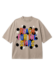 A beige short-sleeve t-shirt with a colorful graphic on the front that reads 'REACH FOR THE STARS' in multicolored letters, surrounded by black dots and white stars