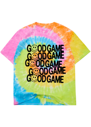 A vibrant tie-dye t-shirt featuring a spiral pattern of pink, orange, yellow, green, and blue, with the text 'GOOD GAME' and a smiley face printed repeatedly in black across the chest