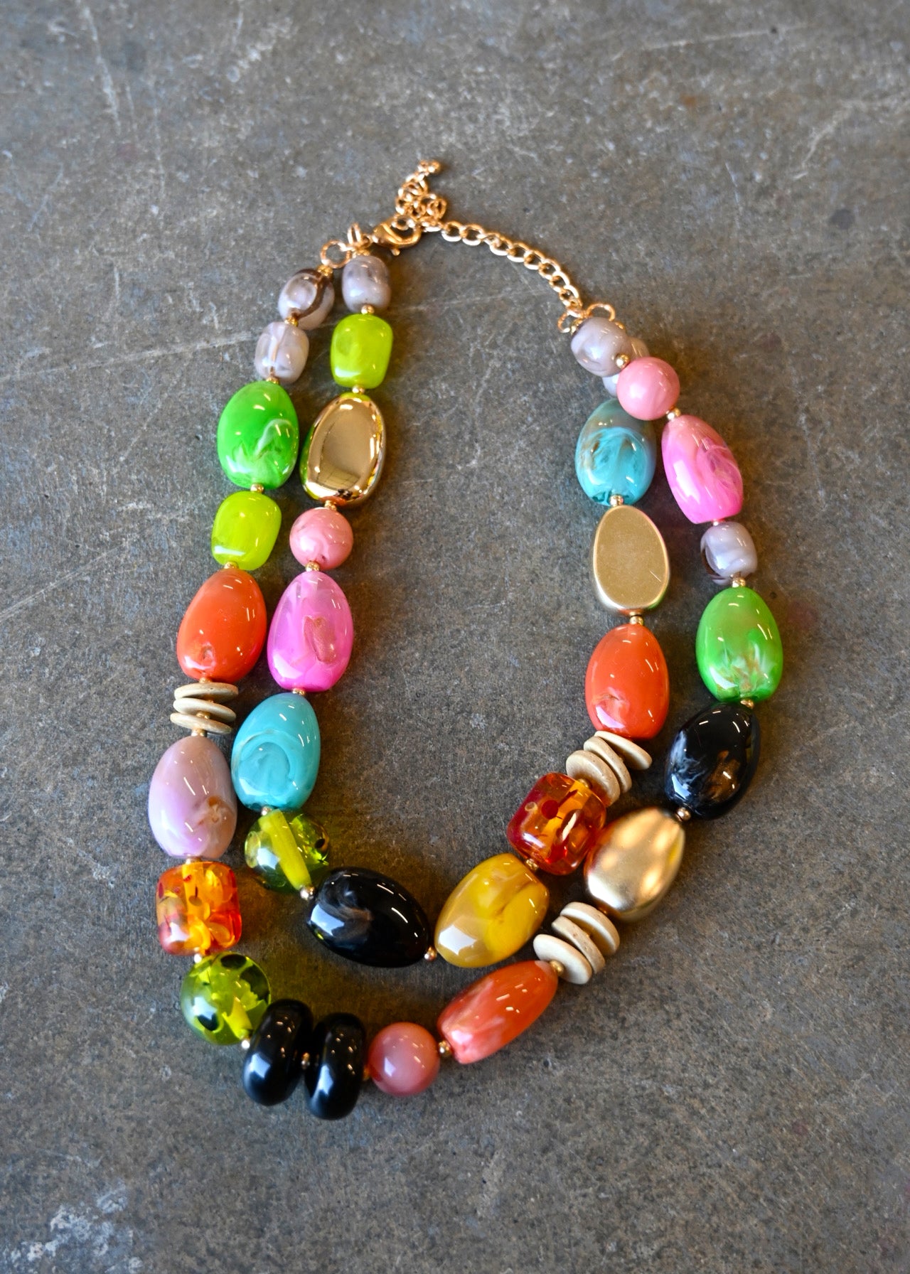 A gold chain necklace with multicolored beads in various shapes on a dark background