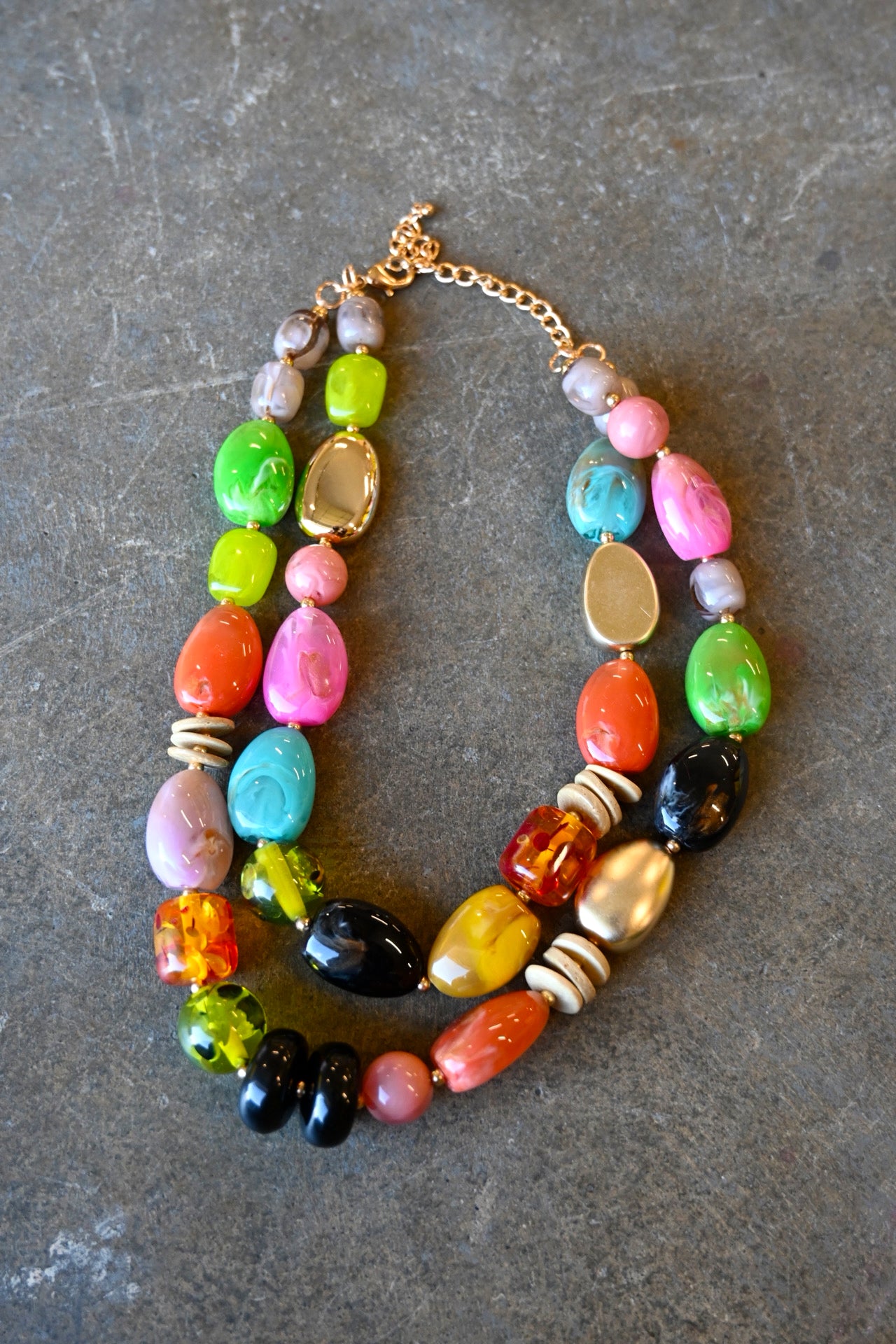 A gold chain necklace with multicolored beads in various shapes on a dark background