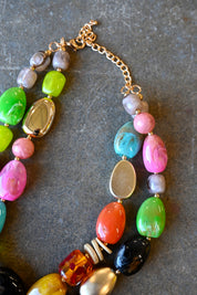 Close up of a gold chain necklace with multicolored beads in various shapes on a dark background