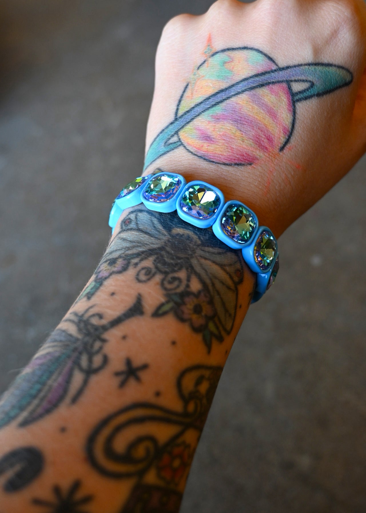 A model's wrist wearing a stretchy bracelet with oval light blue jems on a dark background