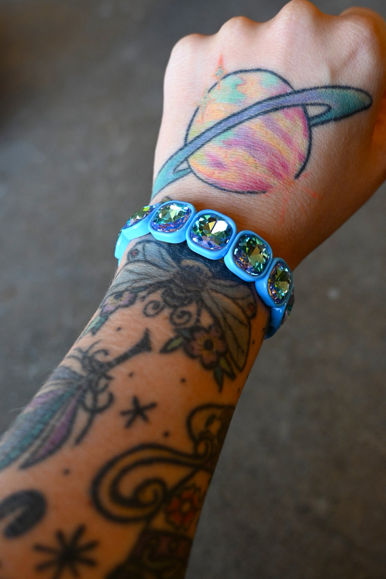A model's wrist wearing a stretchy bracelet with oval light blue jems on a dark background