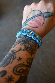 A model's wrist wearing a stretchy bracelet with oval light blue jems on a dark background